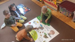 Dzieci siedzą na dywanie i oglądają plansze z kodeksem ekologa.