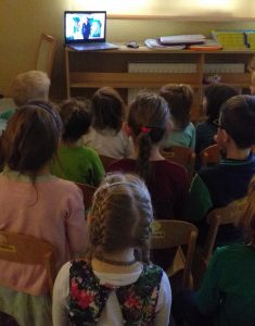 Dzieci siedza przed laptopem i oglądają przedstawienie "Igraszki Czarodziejki Honoratki."