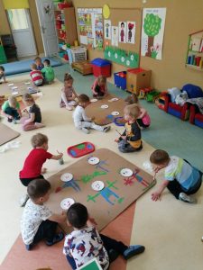 Dzieci z grupy Krasnoludki siedząc na podłodze, malują farbami na dużych arkuszach kartonu