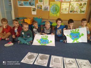 Dzieci na dywanie prezentują plakaty malowane farbami na Dzień Ziemi.